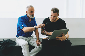 Portrait of two business partners having business conversation as they discussing company sales results presented in the annual report they browsed on a portable computer while sitting in the office.