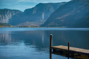 Scenic view of a calm water lake with wooden pier surrounded by mountains in Hallstat, Austria