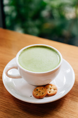 Hot and smooth green tea latte with froth served in white ceramic cup with biscuits