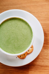 Hot and smooth green tea latte with froth served in white ceramic cup with biscuits