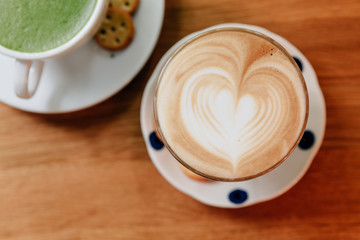 Top view of Latte art heart shape served in clear glass with wooden table in the background. 