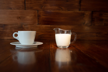 milk in glass milk jug with white cup and reflection from a wooden table