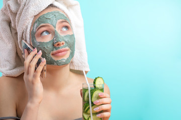 Caucasian woman with towel on head and face mask enriching with cucumbers talking with her friend...