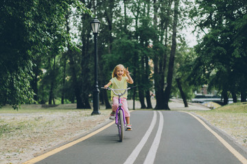 Fototapeta premium little child showing peace sign while riding bicycle on road in park on summer day