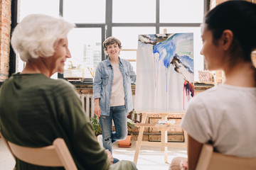 Portrait of modern female artist presenting modern watercolor painting to audience standing in...