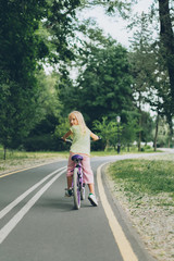 Fototapeta premium back view of kid looking at camera while riding bicycle on road in park