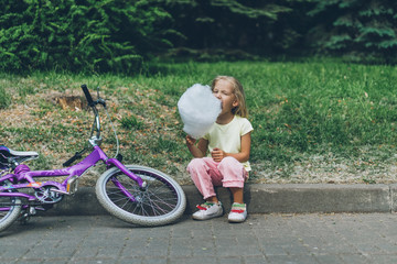 adorable kid with bicycle eating cotton candy in park