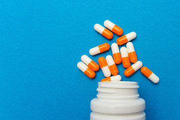 Orange white capsules (pills) were poured from a white bottle on a blue background. Medical...