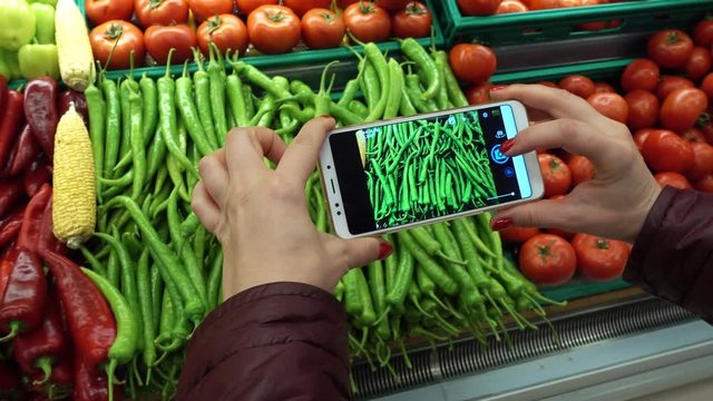 Hand taking picture of tomatoes and other vegetables using smart phone at grocery shop.