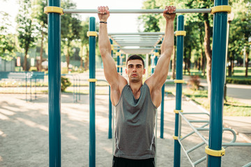 Athlete doing exercise on horizontal bar outdoor