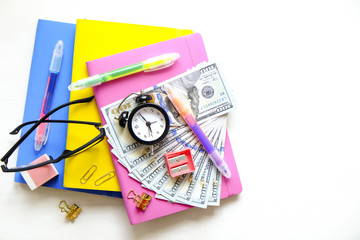 Investing time & money in expensive education, college tuition & fees concept. Pack of new one hundred dollar bills, notebooks, school supplies, alarm clock. Background, copy space, close up, flat lay