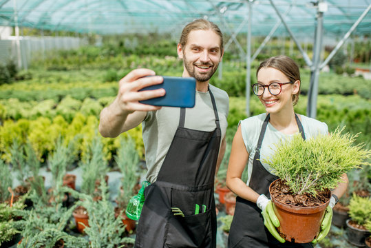 Couple of gardeners making selfie photo standing together with plant in the greenhouse