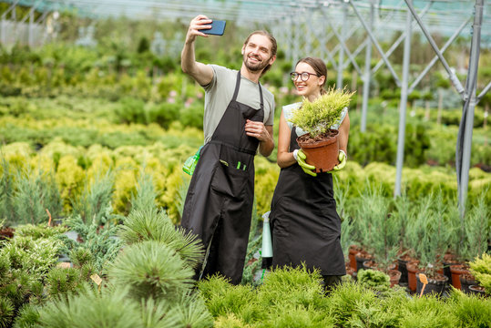 Couple of gardeners making selfie photo standing together with plant in the greenhouse