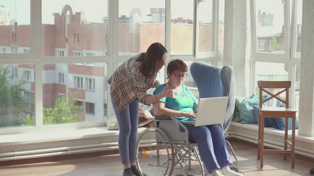 Woman in a wheelchair holding a laptop next to a colleague girl