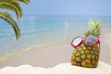 pineapple with sunglasses in the summer landscape on the beach