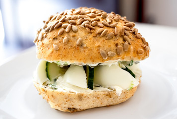 Healthy vegetarian egg and cucumber bread roll with sunflower seeds on white plate.