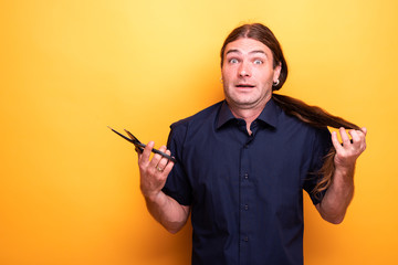 Man with despaired look thinking of cutting hair with scissors