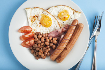 Plate of breakfast with fried eggs, bacon beans tomatoe slices isolated on blue background