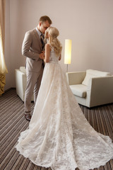 Fototapeta premium Groom is kissing a bride in luxury wedding dress with plume, before wedding ceremony, at the hotel room.
