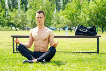 A handsome young man without a T-shirt is engaged in yoga and Pilates in the park. Exercise outdoors