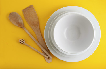 Big stack of different white plates, bowls, isoalted yellow background, one above the another.Wooden Spoons, Copy Space.