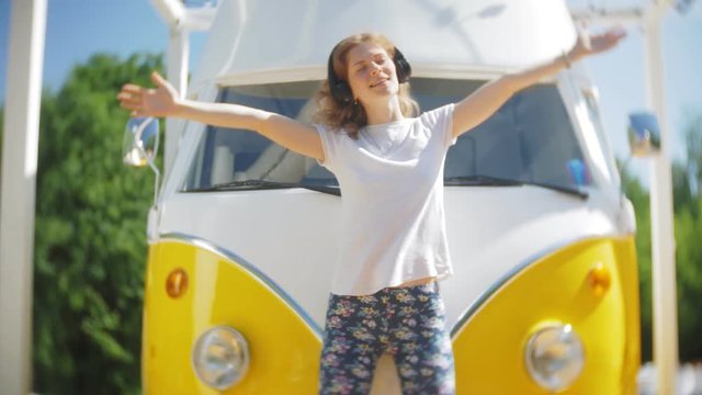 young woman outdoors by yellow vagon car listening music in headphones using smartphone - relaxing, enjoying, concept of technology and travel