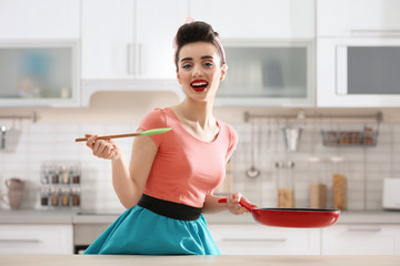 Funny young housewife with spoon and frying pan in kitchen