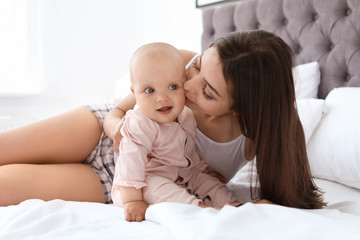 Young mother with her cute baby girl on bed at home