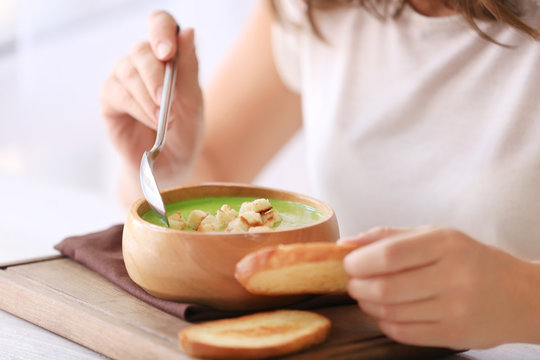 Woman eating tasty spinach soup in kitchen
