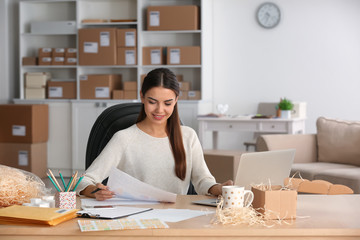 Young woman with laptop preparing parcels for shipment to client in home office