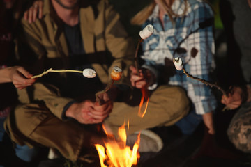 Friends frying marshmallows on bonfire at night, closeup. Camping season