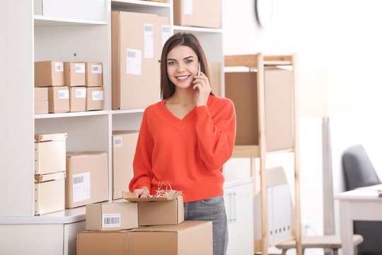 Young woman with mobile phone preparing parcels for shipment to client in home office