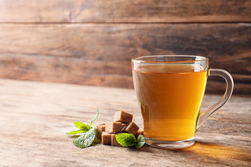 Cup with hot aromatic mint tea, fresh leaves and sugar cubes on wooden table