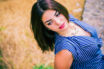 Fototapeta premium Portrait of a brunette girl with brown eyes in a blue striped dress