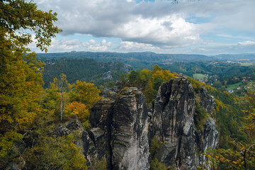Fototapeta na wymiar Scenic autumn landscape of rocky mountains and forest with colorful trees in Saxon Switzerland National Park on cloudy day. Germany
