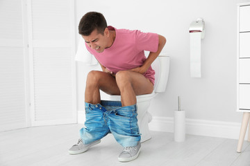 Young man suffering from diarrhea on toilet bowl at home