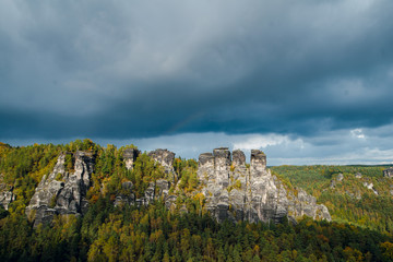 Fototapeta na wymiar Wonderful Autumn landscape of rocky mountains and forest with colorful trees in Saxon Switzerland National Park on cloudy day. Before the rain and storm. Germany