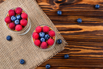Healthy blueberry and raspberry parfait in a glass on a rustic brown wood background. Two portions. Space for text or design.