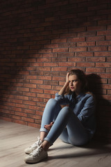 Fototapeta na wymiar Depressed young woman sitting on floor near brick wall