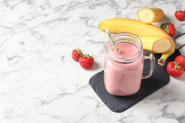 Mason jar with tasty strawberry smoothie on marble table