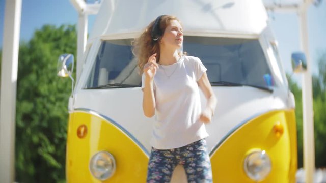 young woman outdoors by yellow vagon car listening music in headphones using smartphone - relaxing, enjoying, concept of technology and travel