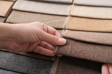 Young woman choosing among upholstery fabric samples, closeup. Interior design