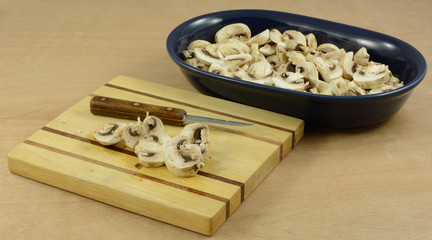 Preparing to cook by chopping mushrooms on wooden cutting board and putting in blue ingredient dish