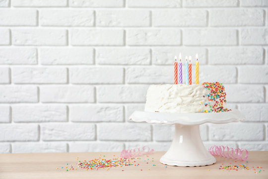 Birthday cake with candles on table against brick wall