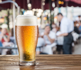 Frosty glass of light beer on the bar counter in the open-air cafe.