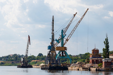 Heavy cranes in cargo port on the riverbank