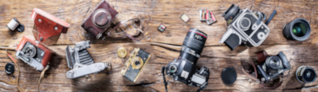 Blurred Panoramic Picture Of Different Photo Cameras On Wood.