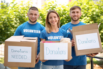 Young volunteers holding boxes with donations for poor people outdoors