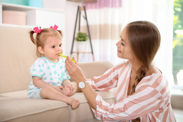 Caring mother feeding her cute little baby with healthy food at home