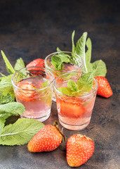 Homemade Strawberry liqueur on a metal table. Alcoholic fruit cocktail shots in a glasses. Green leafs